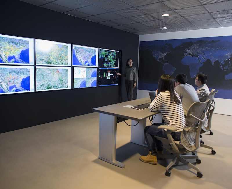 Photo of several people sitting at desk looking at screens with maps