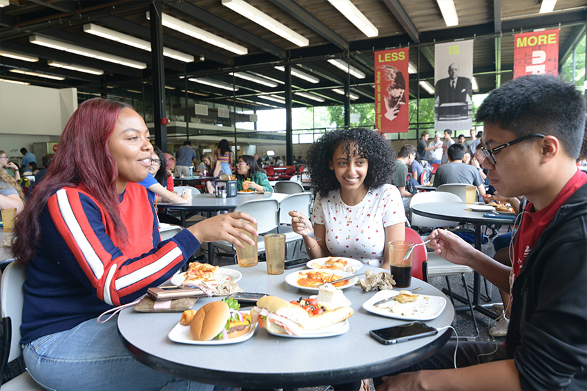 Three students eat around a table in the Commons