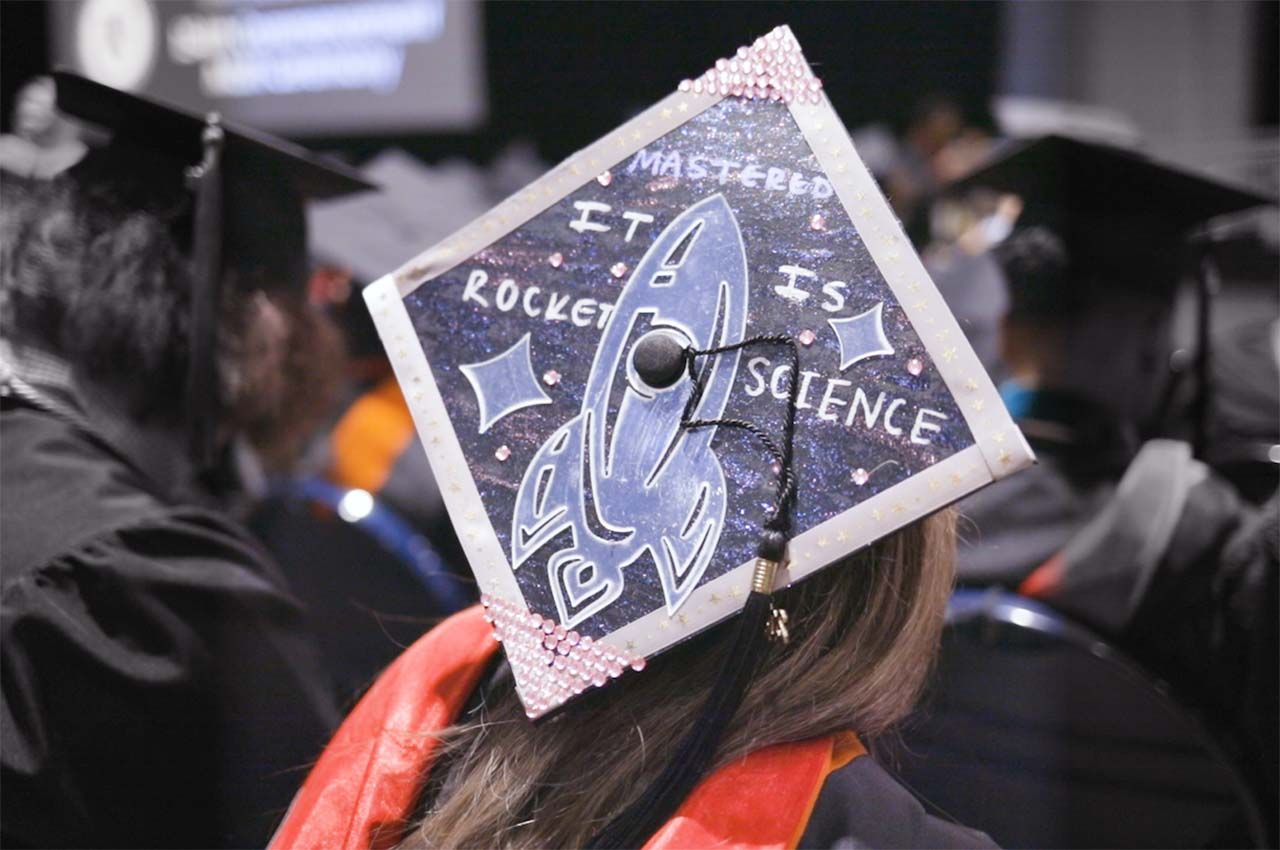 A student's cap at Commencement has a drawing of a rocket and says It Is Rocket Science