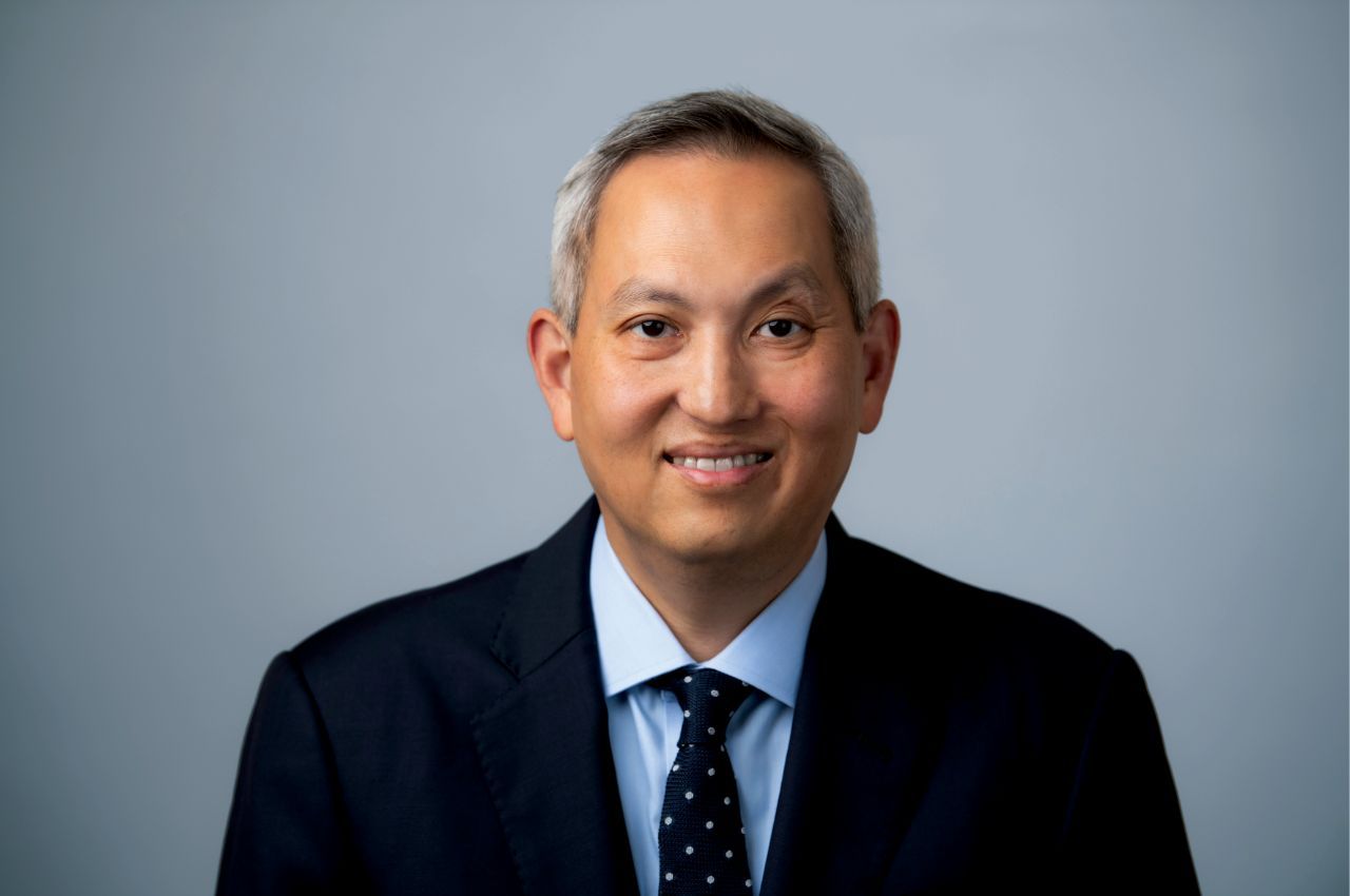 A man wearing a dark suit and tie smiles in a portrait.