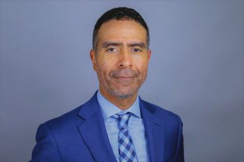 A main in a blue suit and tie smiles in a portrait.