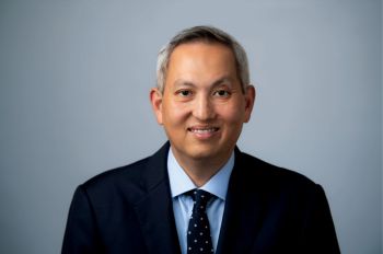 A man wearing a dark suit and tie smiles in a portrait.
