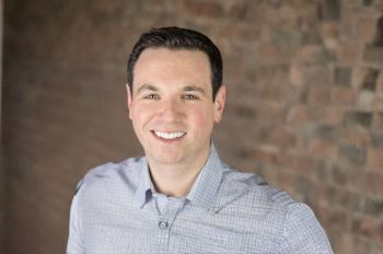 A man wearing a button-down shirt smiles in a portrait.