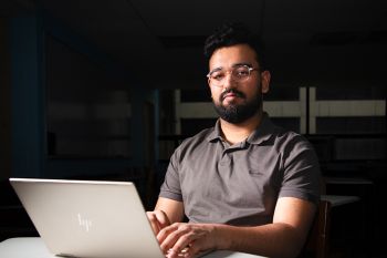 Environmental shot of College of Computing 2026 graduating student Abdul Hadi Khan sitting with computer