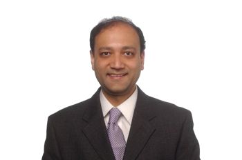 A man in a dark suit smiles for a portrait in front of a white background.