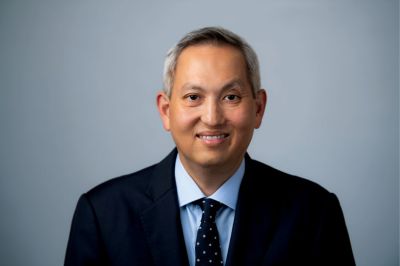 A man wearing a dark suit and tie smiles in a portrait.