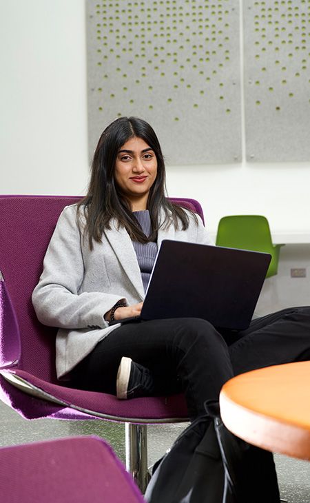 Photo of Sanjana Waghray  (M.A.S. DSC 2nd Year) sitting on a purple chair with a laptop on her lap.