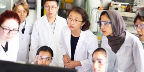 Photo of students and faculty in biology lab gathered around computer monitor