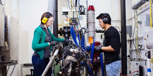 Photo of Carrie Hall and student working on an engine in the lab