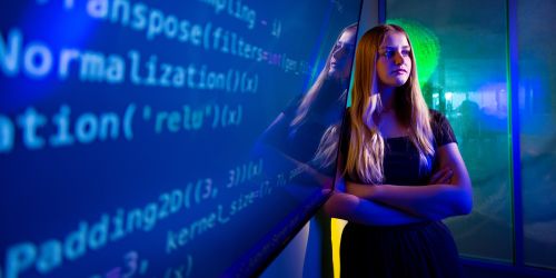 Illinois Tech alumna Maggie Barclay stands next to a monitor with computer code on it