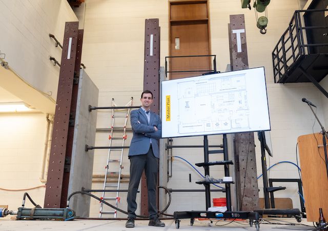 Assistant Professor of Civil Engineering Matthew Gombeda stands in front of the master plan for the Concrete Materials and Structures Lab.