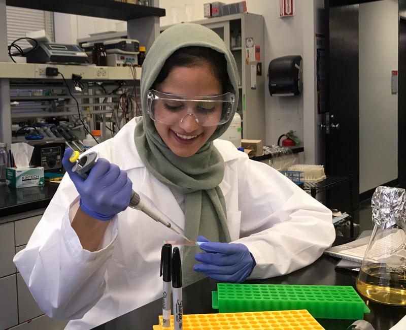 Photo of Anam Adil with pipette in a lab